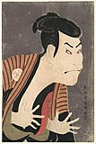 Colour print of a colourfully made-up Japanese actor making a bold expression with his fingers extended, facing right.
