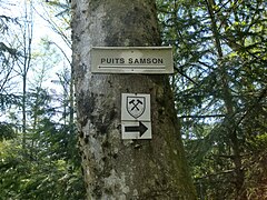 Panneau portant la mention « puits Samson » et une flèche dirigée vers la gauche tandis que le sentier minier est indiqué vers la droite.