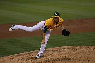 Un joueur de baseball habillé en jaune terminant de lancer la balle.