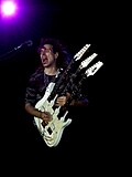 Steve Vai en concert avec sa guitare à triple manche.