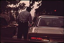 A Metropolitan Police Department of the District of Columbia officer ticketing a motorist for a traffic violation, 1973 DRIVER GETS TICKET FOR JUMPING THE LIGHT - NARA - 546661.jpg