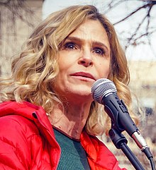 Closeup of a woman's face speaking into a microphone, her eyes are looking out into a crowd