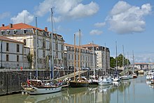 Bâtiments anciens alignés sur un quai. Au premier plan, bateaux de plaisance amarrés au quai.