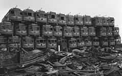 Photographie ancienne en noir et blanc d'une casse automobile où des rames de tramways sont empilées sur plusieurs niveaux.