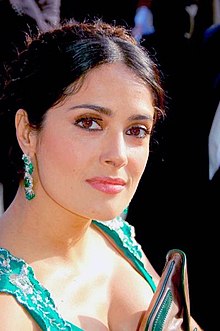 Head and shoulders shot of Hayek looking right, wearing emerald earrings with matching dress