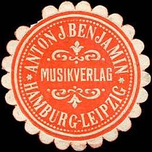 Eine kreisrunde Marke mit rundlicher Zähnung. Auf orangefarbenem Grund steht der Text „Anton J. Benjamin Musikverlag Hamburg-Leipzig“.
