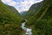 Vallée étroite et boisée avec un torrent en son sein.