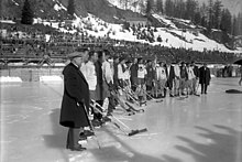 Ice hockey players and staff from two different teams stand together side-by-side in an outdoor ice rink stadium.