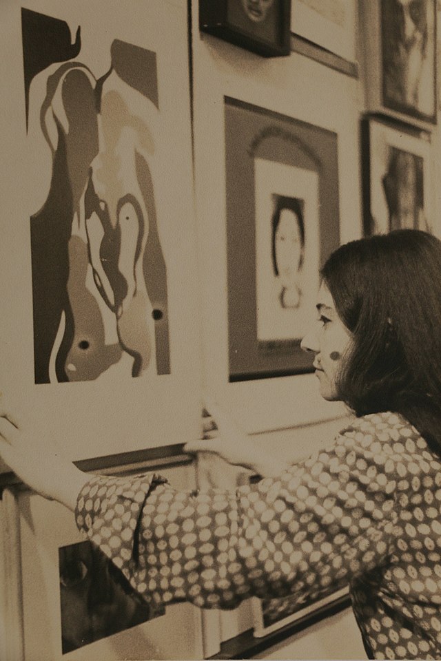 Nisete Sampaio em foto preto e branco de perfil ajusta seu quadro na parede da galeria ao lado de A Bela Lindonéia de Rubens Gerchman.