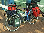 Touring bicycle equipped with head lamp, pump, rear rack, fenders/mud-guards, water bottles and cages, and numerous saddle-bags.