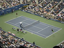 Two men playing on a blue and green hard court, surrounded by crowded bleachers