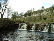 Wain Wath Force, near Keld, with the limestone cliffs of Cotterby Scar in the background.