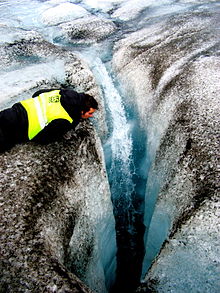photo d'une crevasse dans un glacier dont les surfaces sont recouvertes de particules noires.