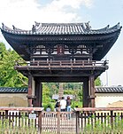 Photo couleur d'une porte en bois à deux étages d'un temple bouddhique, sous un ciel bleu nuageux.