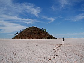 A metal sculpture in front of a hill surrounded by salt flats