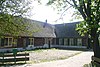 Boerderij. Grote hoeve met puntgevel, waarin ontlastingsbogen. Links een uitgebouwde opkamer. Stal met oude kozijnen en luiken