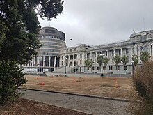 A pathway and soil where there was once lawn with New Zealand's Parliament buildings in the background framed by trees