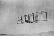 photo N&B d'un planeur biplan, avec deux dérives, piloté par un homme allongé sur le ventre.