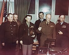 Six smiling and laughing men and one woman in uniform. Eisenhower is brandishing a pen.