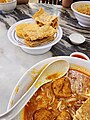 Image 92A bowl of curry mee, with fried beancurd skins and fish cake on the side (from Malaysian cuisine)