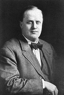 Photograph of an overweight, balding man, seated, facing slightly to his right