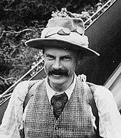 Schwarzweiß Porträt von Mannering 1895. Er trägt einen schwarzen Schnauzer, lächelt und hat einen Hut auf.