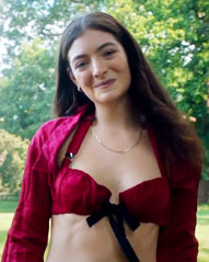 Lorde looks forward with her head on a slight tilt. She is wearing a crimson blouse, with her midriff shown.