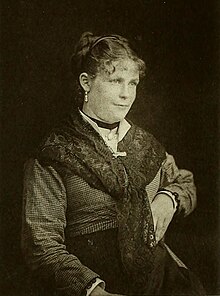 A black-and-white portrait of a young woman wearing a checkered dress and a shawl