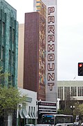 Фотография высокого знака и мозаики, на которой возвышается театр Paramount, возвышающийся над шатром и оживленной улицей.