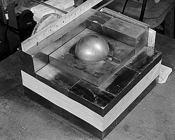 A re-creation of the 1945 criticality accident using the Demon core: a plutonium pit is surrounded by blocks of neutron-reflective tungsten carbide. The original experiment was designed to measure the radiation produced when an extra block was added. The mass went supercritical when the block was placed improperly by being dropped. Partially-reflected-plutonium-sphere.jpeg
