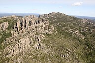 An aerial view of a rocky hillside partly covered by green and yellow vegetation.