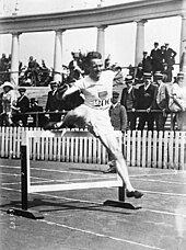 Photo d'un homme venant de sauter par dessus un obstacle ou haie.