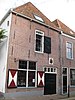 Voormalig wachthuis. Gepleisterd bakstenen gebouw met schilddak. Twee leeuwenmaskers. Gevelsteen met het wapen van Edam aan de Hoogstraat