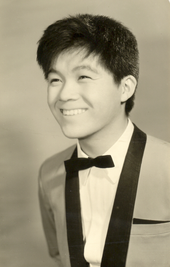 A young East Asian man wearing a tuxedo and smiling broadly