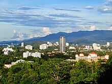Photographie panoramique des gratte-ciel et autres immeubles de la ville de Kota Kinabalu dépassant la cime des arbres de la forêt tropicales qui les entoure.