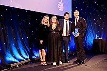 Colour photograph of members the ITV News team posing onstage with their AIB award.