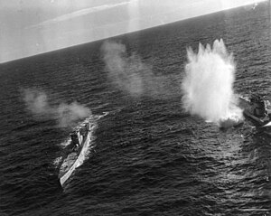 An angled photo of two submarines with bomb splashes around them
