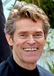 Willem Dafoe smiling for a photograph at the 2019 Cannes Film Festival.