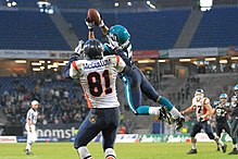A defensive player leaps into the air in front of a receiver and intercepts the pass