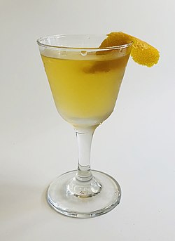 A deep yellow cocktail in a cocktail glass, garnished with an orange peel.