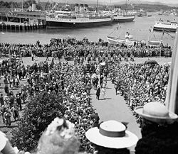 A crowd in Victoria, British Columbia, watch King George VI and his royal consort, Queen Elizabeth, coming up the walkway during their 1939 royal tour of Canada His Majesty King George VI and Her Majesty Queen Elizabeth coming up the walkway with a view of the harbour of Victoria in the background.jpg