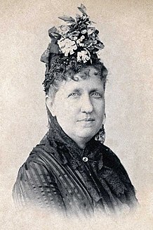 Head and shoulders photograph of a middle-aged Isabel wearing a flower hat