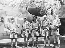 Five men in tropical military uniforms stand beside rear fuselage and turret of Lockheed Hudson bomber