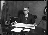 Photographie en noir et blanc d'un homme assis à son bureau.