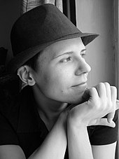 Kateryna Michalizyna ist auf einer schwarz-weiß Fotografie im seitlichen Porträt abgebildet. Sie hält die Hände unter dem Kinn und trägt einen Hut.