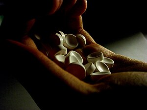 English: a hand holding unidentified white pills