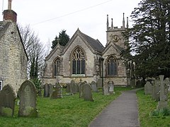 Gray three bay building with arched windows. Tower behind and gravestones in the foreground.