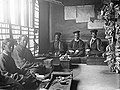 The police court. The magistrates are in overcoats and caps, with their clerks. Court records are fastened to walls and pillars.