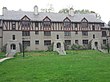 A three-story Tudor-style building stands before a green lawn on an overcast day.