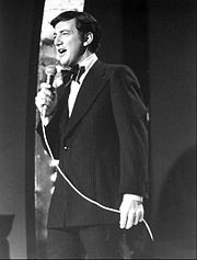 A black and white image of a man in a suit holding a microphone